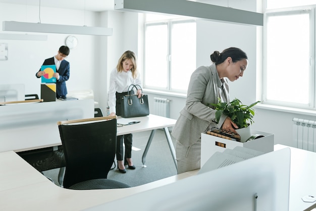 Tres jóvenes gerentes de oficinas interculturales que regresan a sus lugares de trabajo y se paran junto a sus escritorios y dejan papeles y suministros