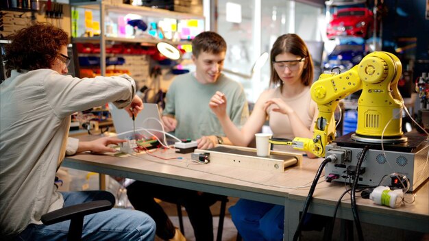 Tres jóvenes ingenieros felices arreglan un brazo robótico amarillo en el taller de programación de computadoras