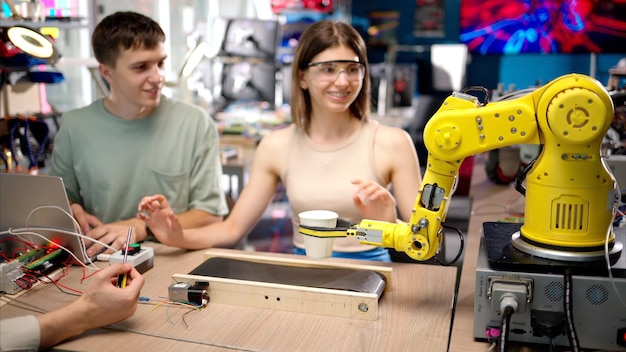 Tres jóvenes ingenieros felices arreglan un brazo robótico amarillo en el taller de programación de computadoras