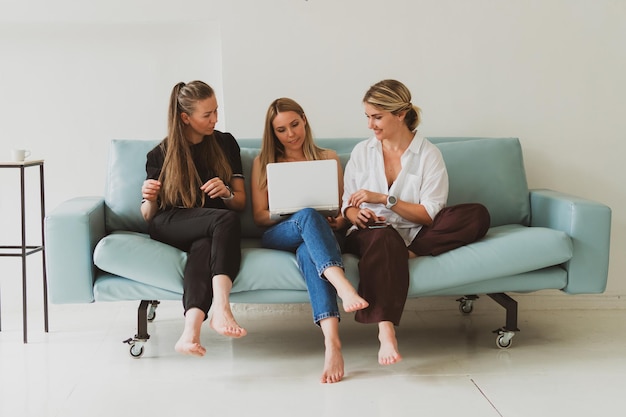 Tres jóvenes mujeres atractivas en casa en el sofá hablando mientras miran la computadora portátil