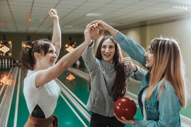 Tres jóvenes mujeres felices están celebrando su puntuación en el club de bolos.