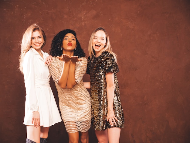 Tres jóvenes mujeres morenas hermosas internacionales en vestido brillante de verano de moda.