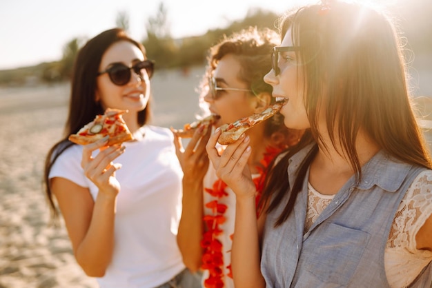 Tres jóvenes pasando tiempo juntas en la playa haciendo un picnic comiendo pizza