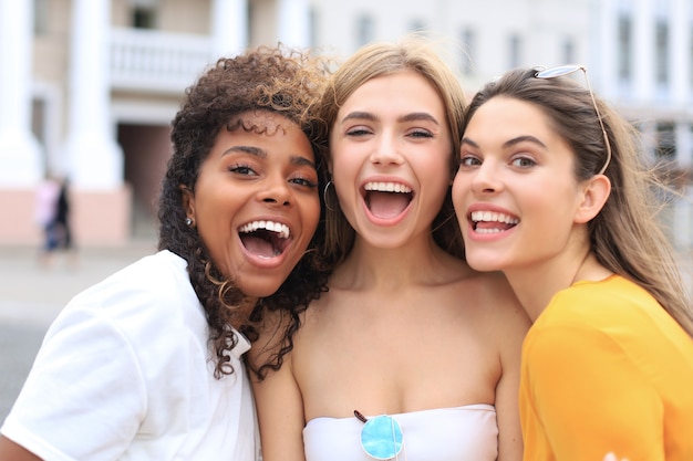 Tres jóvenes sonrientes hipster mujeres en ropa de verano posando en la calle. Mujer mostrando emociones positivas en la cara.