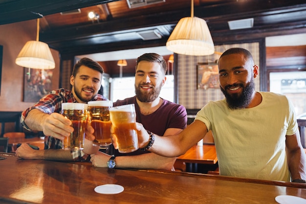 Três jovens amigos bonitos e sorridentes bebendo cerveja em um bar juntos