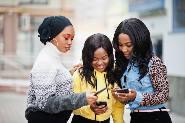 Três jovens amigos da mulher afro-americana com telefones celulares.