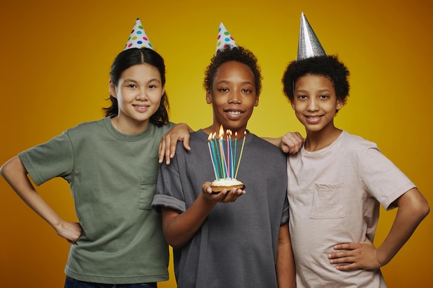 Três jovens amigos multiculturais em bonés de aniversário e roupas casuais em frente à câmera whi