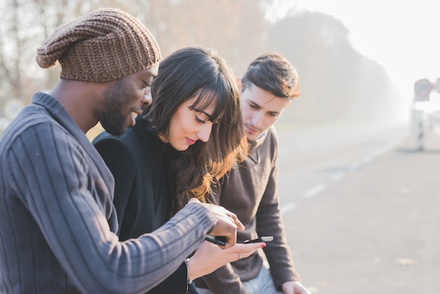 Três jovens amigos multiétnicas ao ar livre usando smartphone