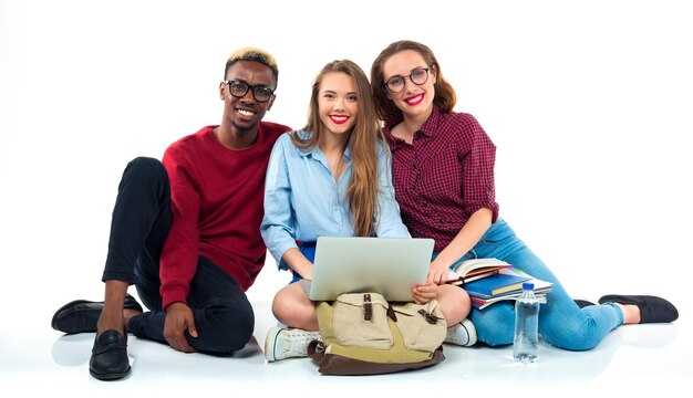 Foto três jovens estudantes adolescentes felizes sentados com livros, laptops e sacos isolados em fundo branco