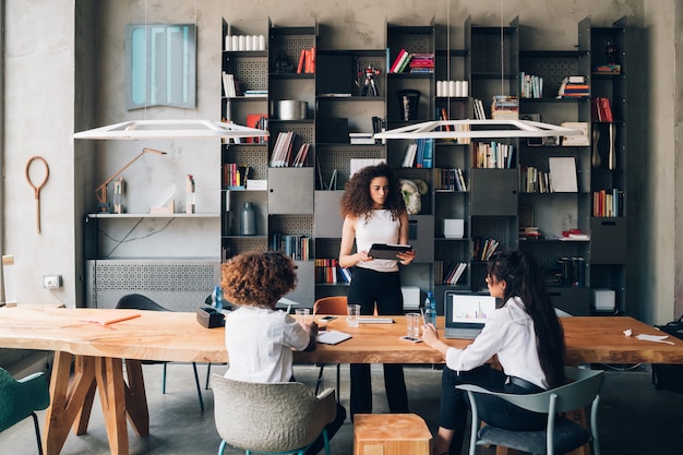 Três jovens estudantes multiculturais discutindo projeto no escritório de coworking com o professor