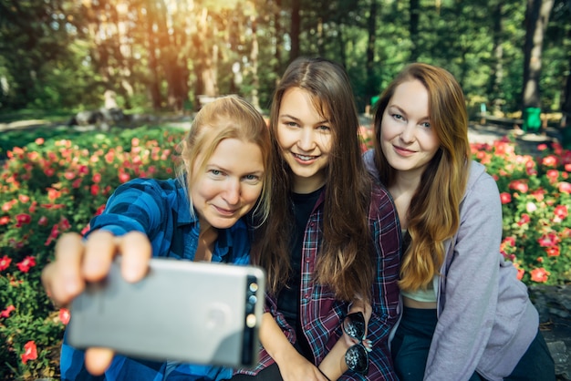 Três jovens garotas bonitas tomando selfie em smartphone no parque de verão.