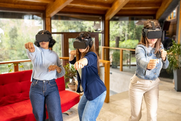 Três jovens mulheres desfrutam de realidade virtual na sala de estar amigas usando novas tecnologias para jogos simulados movimentos de artes marciais com fones de ouvido para realidade aumentada