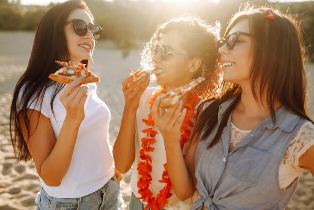 Três jovens passando tempo juntos na praia fazendo piquenique comendo pizza