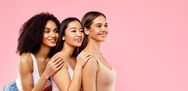 Três jovens senhoras multiétnicas em pé na fila e olhando de lado para o espaço livre posando em rosa