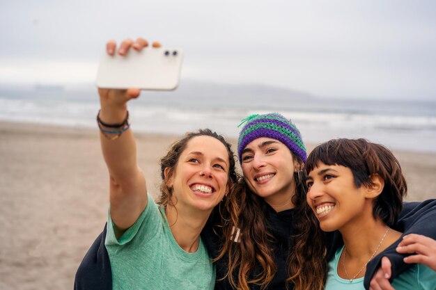Três jovens sorridentes tomando selfie na praia