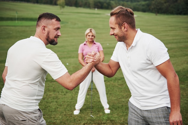 Tres jugadores juegan en el campo de golf. El equipo felicita y se da la mano.