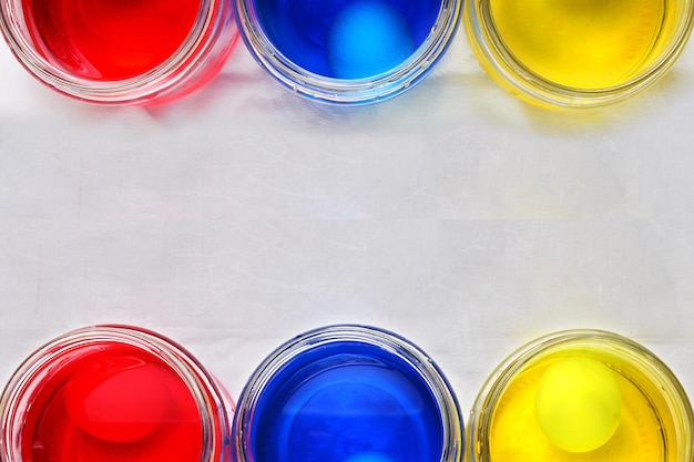 Foto tres latas de vidrio con colores para los huevos de pascua y cinco huevos de gallina blancos esparcidos