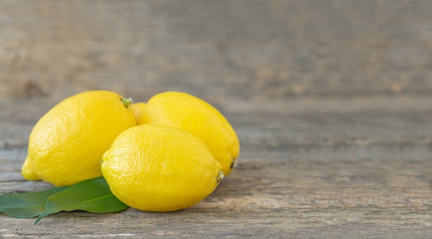 Tres limones amarillos con hojas verdes sobre una superficie de madera