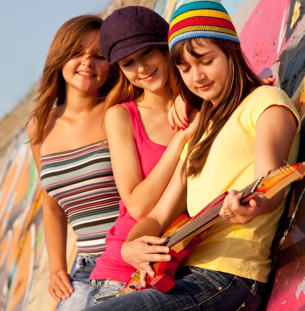 Três lindas garotas com guitarra e parede de graffiti