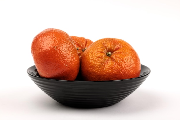 Foto tres mandarinas en un frutero negro sobre un fondo blanco.