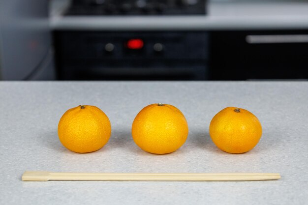 Tres mandarinas sobre una mesa blanca sobre un fondo oscuro de cocina