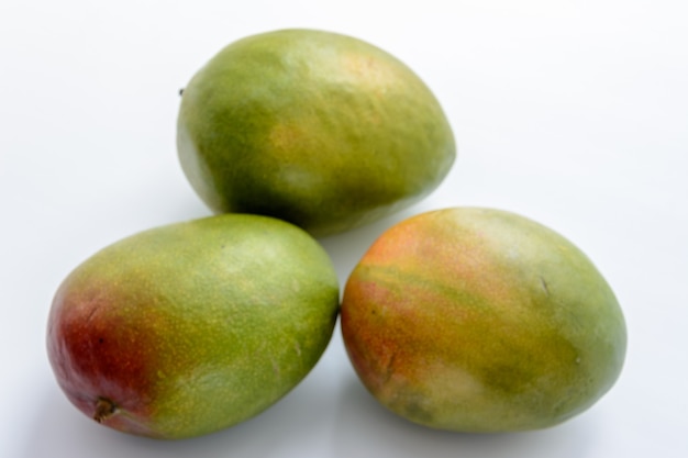 Três mangas maduras em um fundo branco. As mangas são frutas suculentas de caroço (drupa) de numerosas espécies de árvores tropicais pertencentes ao gênero Mangifera. Fruta tropical.