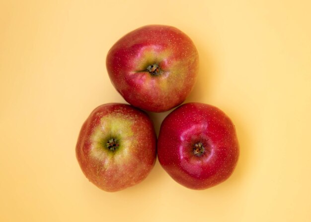 Tres manzanas rojas yacen sobre un fondo amarillo