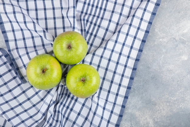 Tres manzanas verdes saludables con mantel sobre la superficie de piedra.