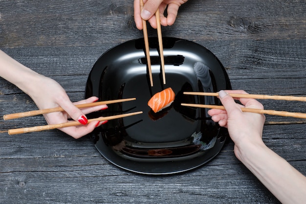 Três mãos com pauzinhos e sushi.