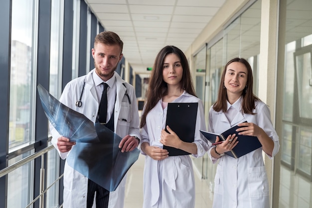 Tres médicos internos mirando a través de la imagen de rayos X de los pulmones para la neumonía viral del paciente Covid-19 en la clínica. Concepto medico