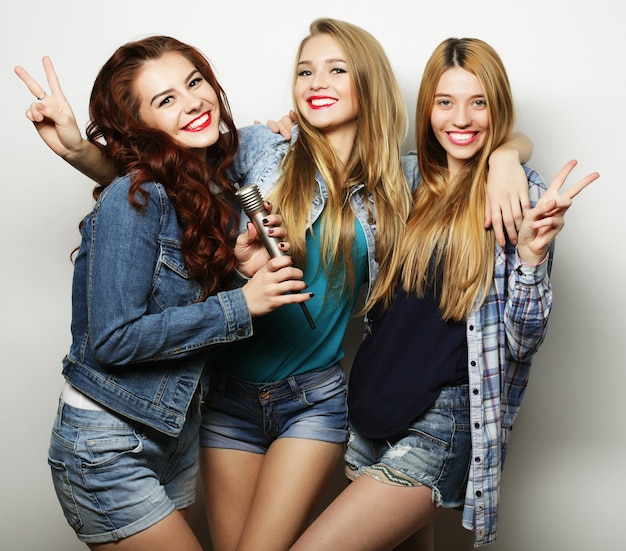 Tres mejores amigas posando en el estudio, vestidas con ropa de estilo veraniego y pantalones cortos de jeans. Chicas sonriendo y divirtiéndose.