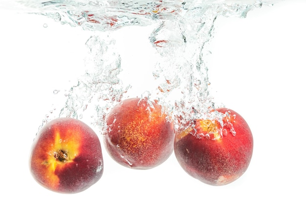 Foto tres melocotones cayendo en el agua con salpicaduras