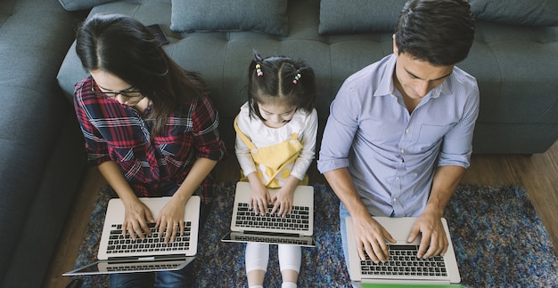 Foto três membros de família diversa, pai caucasiano e mãe asiática e meia filha sentados juntos na sala de estar da casa e usando 3 laptops. ideia para trabalhar em casa.