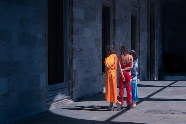 Três meninas de roupas vivas tirando uma selfie no quintal escuro de uma mesquita medieval em Istambul, Turquia