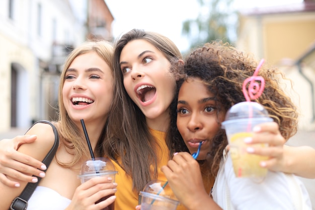 Três meninas na moda hipster legal, amigos bebem coquetel no fundo urbano da cidade.