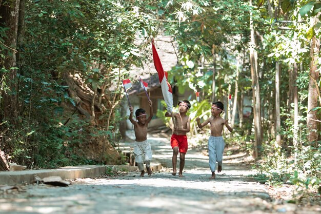 Três meninos correndo sem roupa segurando a bandeira vermelha e branca e levantando