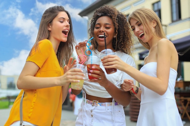 Tres modernas amigas hipster beben un cóctel en el fondo urbano de la ciudad