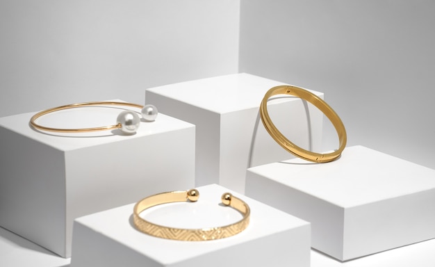 Tres modernas pulseras de oro en cajas geométricas blancas.