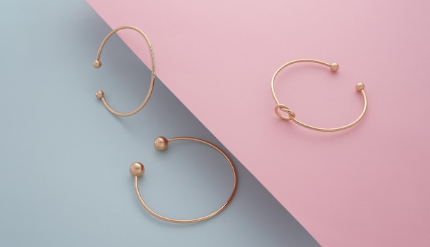 Tres modernas pulseras de oro sobre fondo de papel inclinado rosa y azul