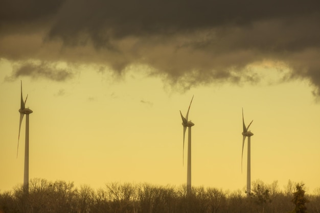Três moinhos de vento em uma paisagem plana com nuvens de chuva escuras e cor amarela