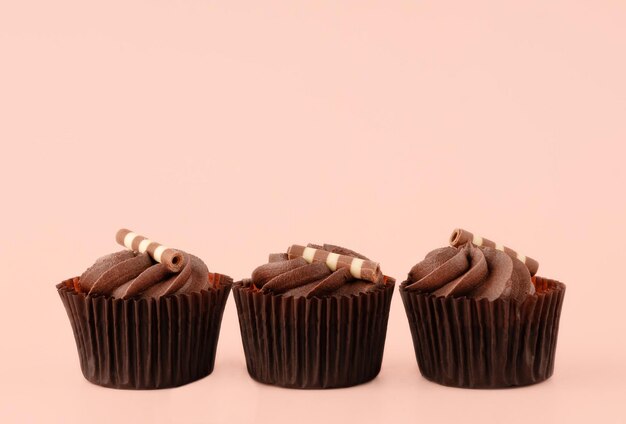 Três muffins de chocolate em embalagens marrons em um fundo rosa