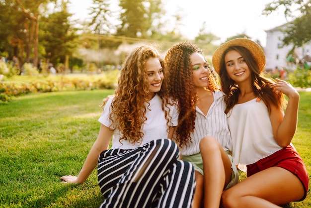 Foto tres, mujer joven, relajante, en, el, grass, jóvenes, amigos, reír, y, el gozar, vacaciones, juntos