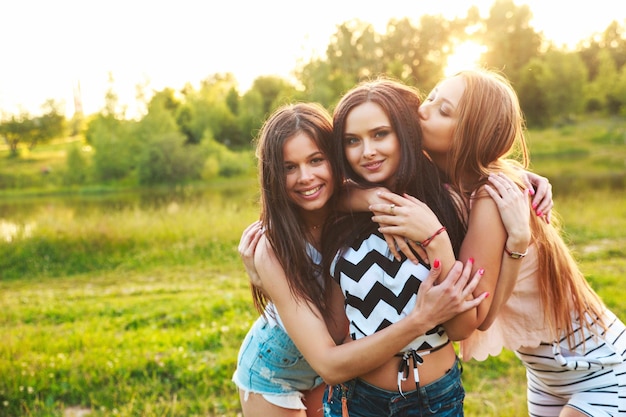 Foto tres mujeres abrazándose al aire libre y riendo al atardecer