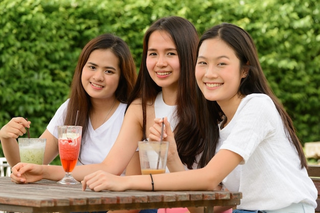 Tres mujeres asiáticas jóvenes felices como amigos tomando una copa juntos en la cafetería al aire libre