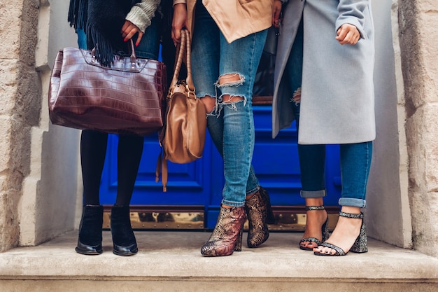 Tres mujeres con elegantes zapatos y accesorios al aire libre. Concepto de moda de otoño. Señoras sosteniendo bolsos femeninos modernos