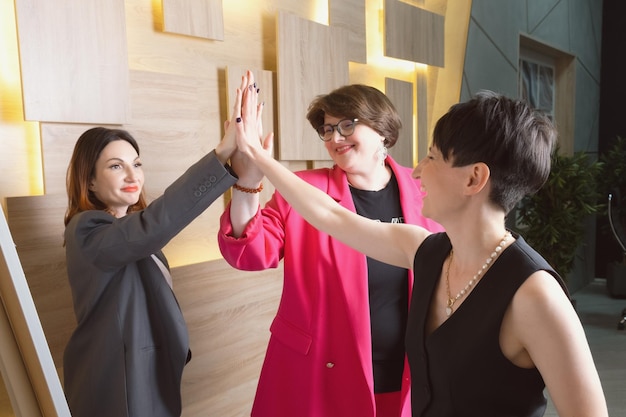 Tres mujeres de mediana edad se dan un highfive en una sesión de capacitación corporativa mujeres reciben capacitación empresarial en grupo