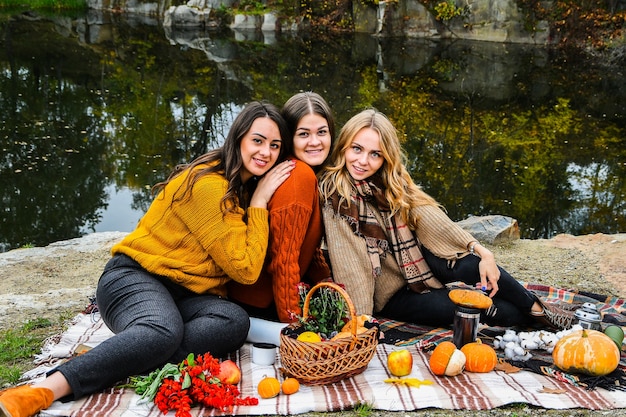 Tres mujeres mejores amigas en picnic de otoño en el parque. Cuadros coloridos, termo y pumpins. Amigos divirtiéndose al aire libre. Cálido día de octubre de otoño