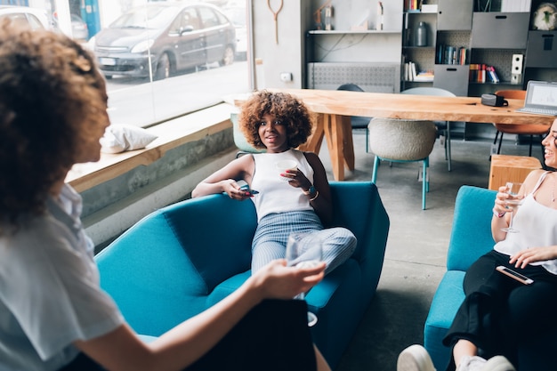 Tres mujeres multirraciales jóvenes sentados en un pub moderno y bebiendo juntos