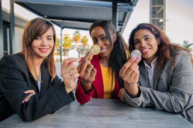 Tres mujeres sostienen tres monedas criptográficas en sus manos durante una reunión de mujeres en la cadena de bloques