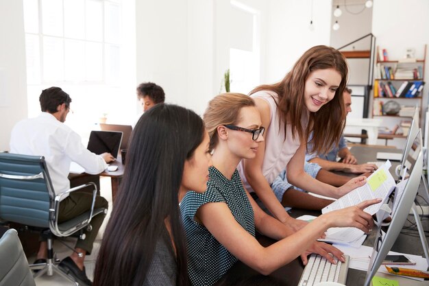 Tres mujeres trabajando juntas en una computadora en una oficina abierta